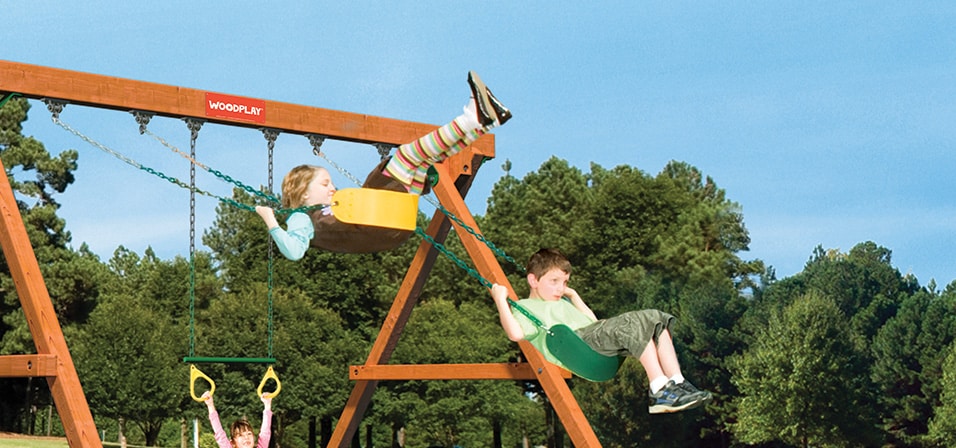 Children Swinging On An Outdoors Wooden Swingset With Slides